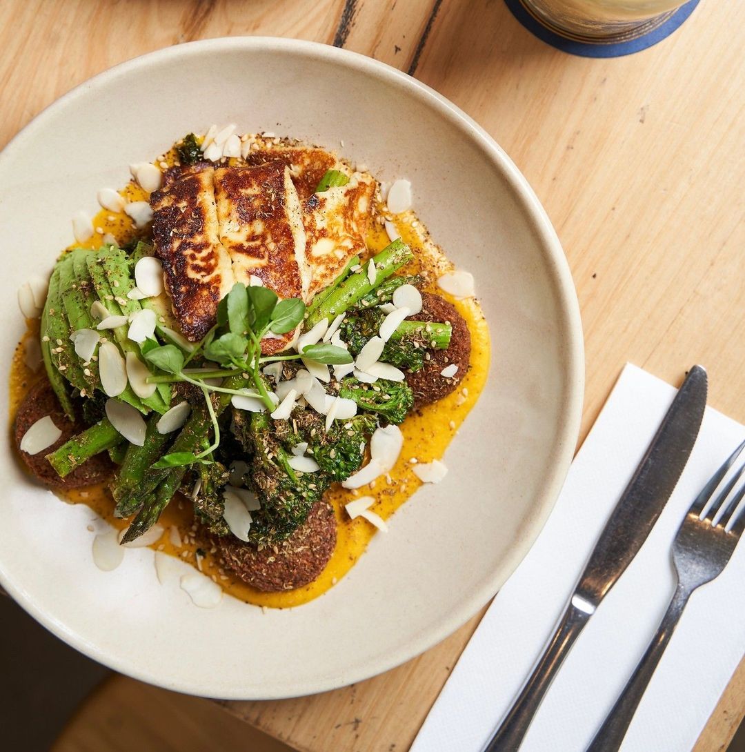 A brunch plate of grilled halloumi, avocado, broccolini and falafel over pumpkin puree