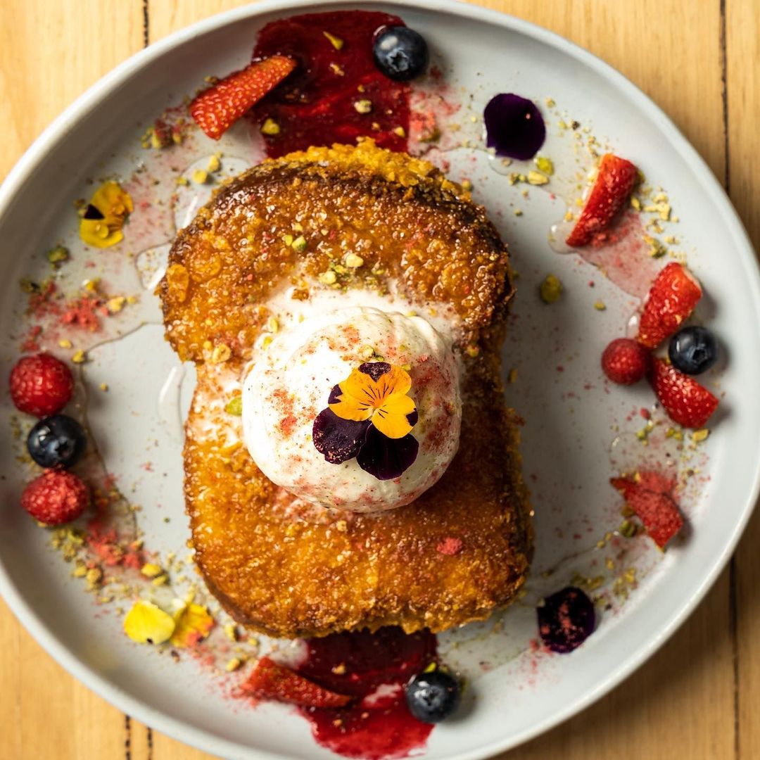 Crumbed French toast plated with berries, pistachio crumb and a scoop of cream