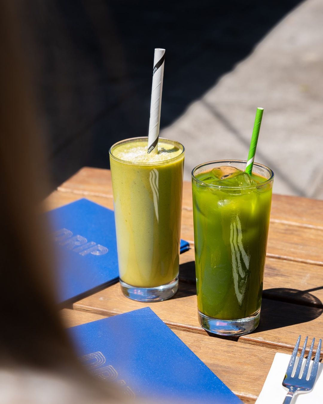 A green smoothie and an iced green juice on a sunlit outdoor table at Drip Cafe