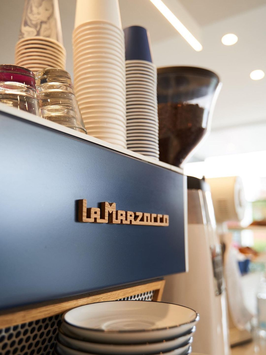 Drip Cafe's navy La Marzocco espresso machine with takeaway cups stacked on top