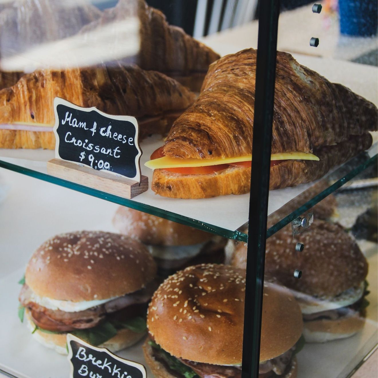 Ham and cheese croissants above breakfast rolls in Drip Cafe's glass pastry cabinet
