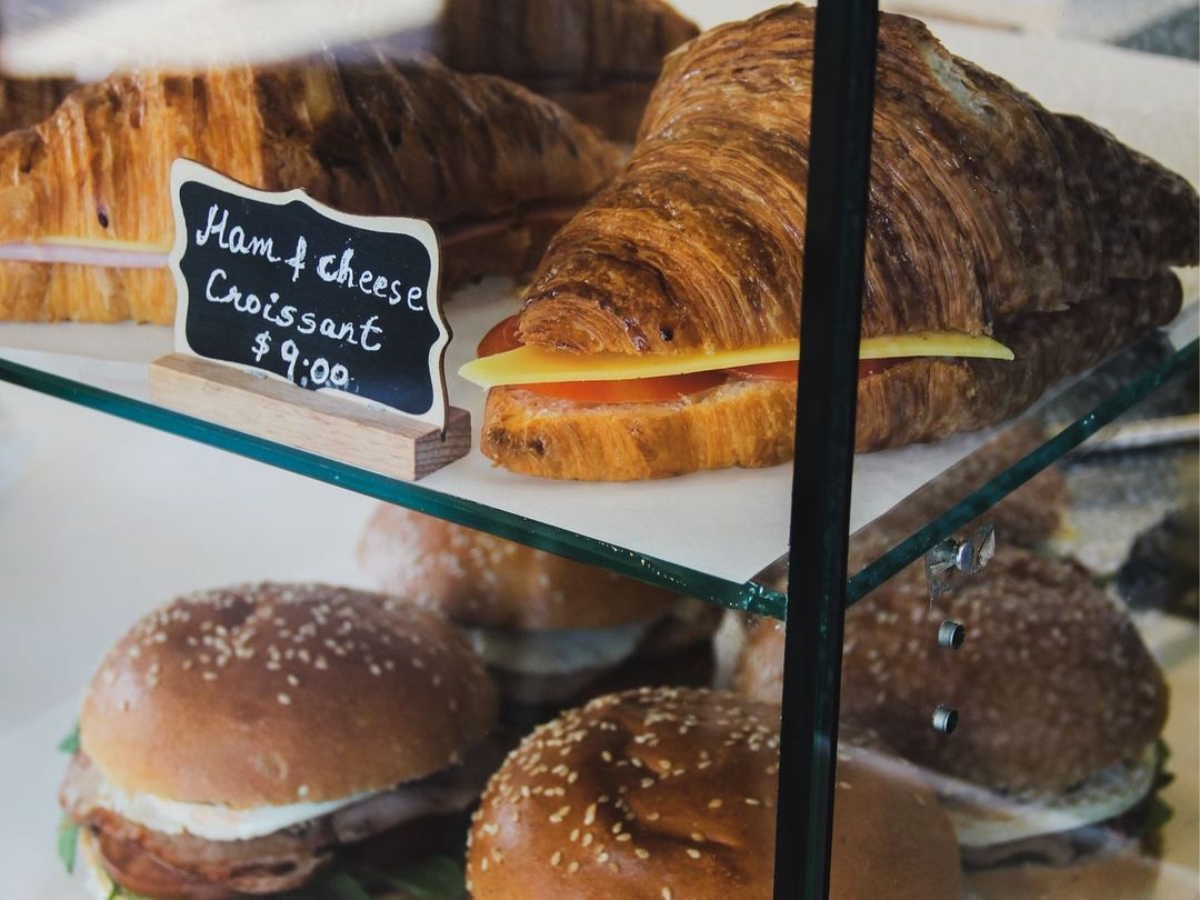 Ham and cheese croissants above breakfast rolls in Drip Cafe's glass pastry cabinet