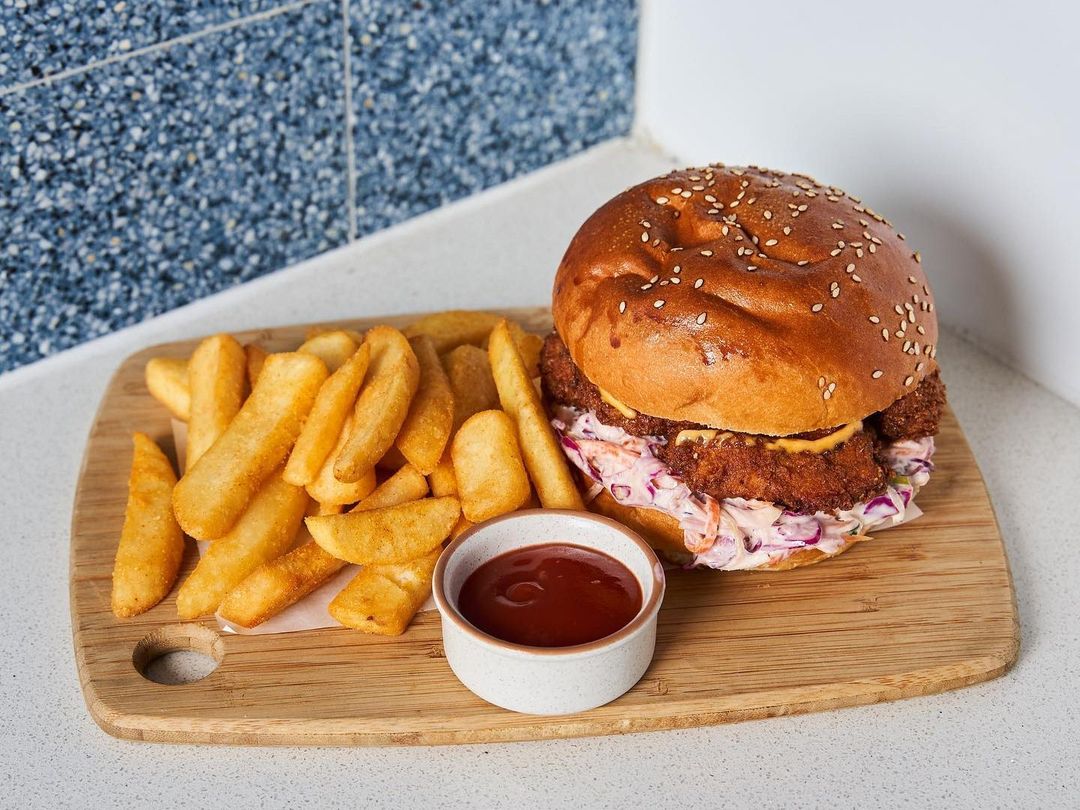 A crispy chicken and slaw burger on a sesame bun with chips and tomato sauce