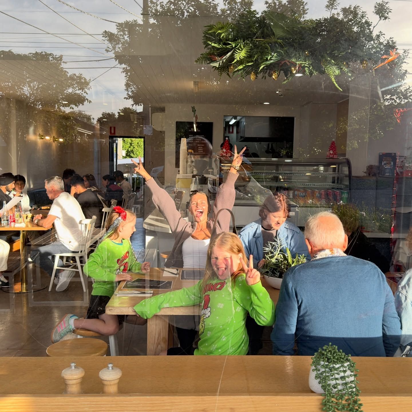A family cheering at a table inside the cafe, seen through the front window