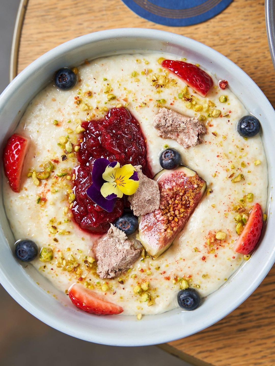 Creamy porridge topped with rhubarb compote, fresh fig, berries and pistachio