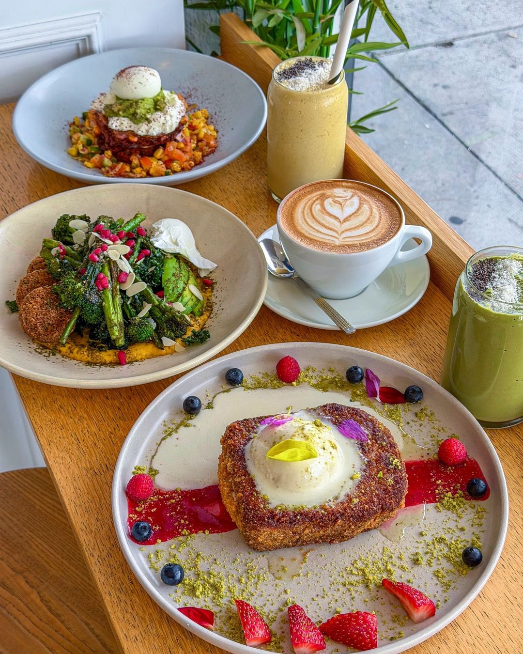 A brunch spread of corn fritters, charred greens and crumbed french toast beside a latte, smoothie and matcha