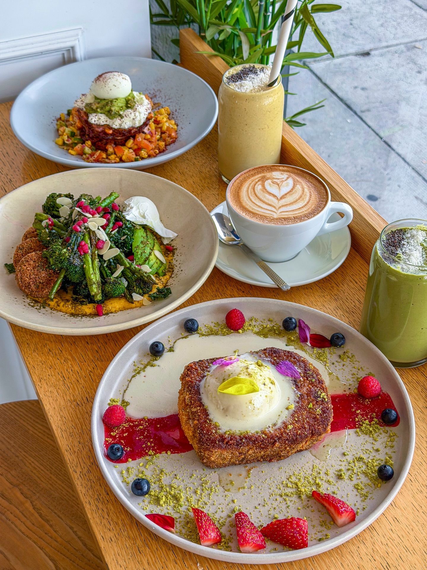 A brunch spread of eggs, broccolini and French toast with a latte, a matcha and a smoothie