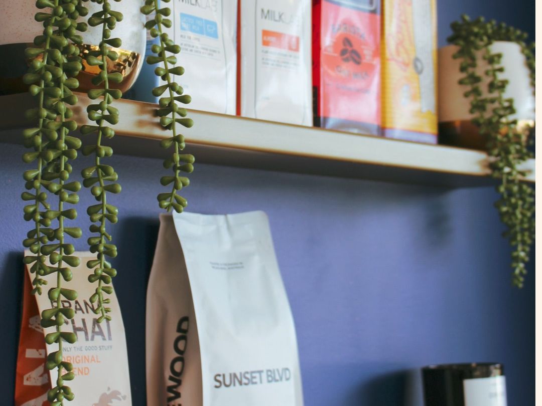 Retail shelves of coffee beans and chai against Drip Cafe's blue feature wall with trailing plants