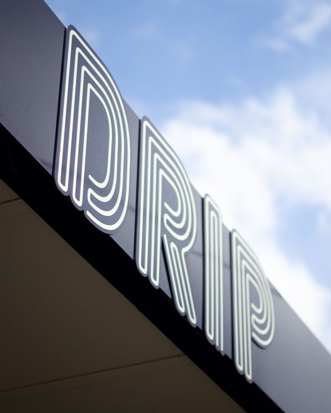 Drip Cafe's illuminated corner sign against a blue Cheltenham sky
