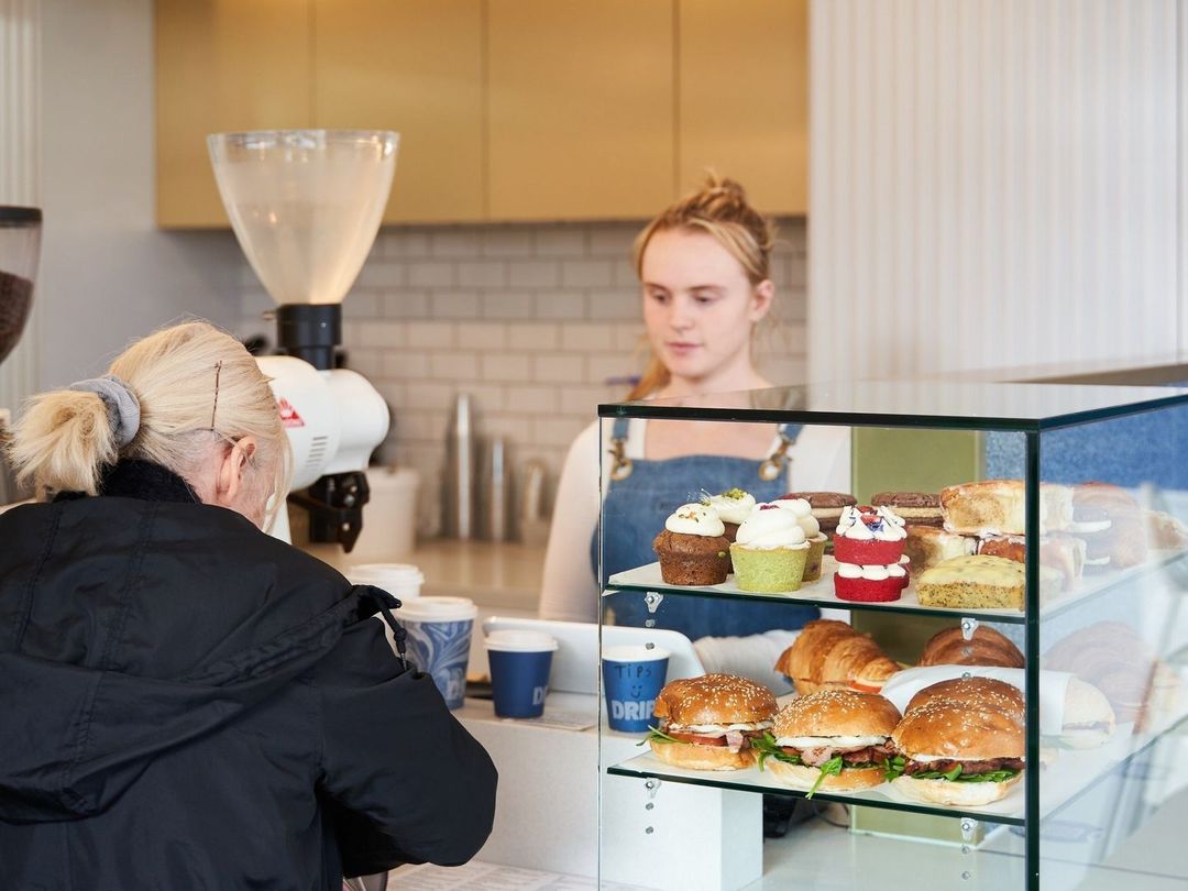 A customer ordering at the Drip Cafe counter beside the pastry cabinet