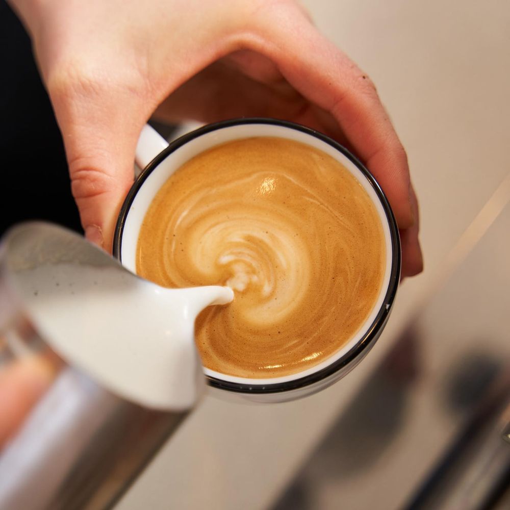 A barista pouring milk into a cup of espresso, seen from above
